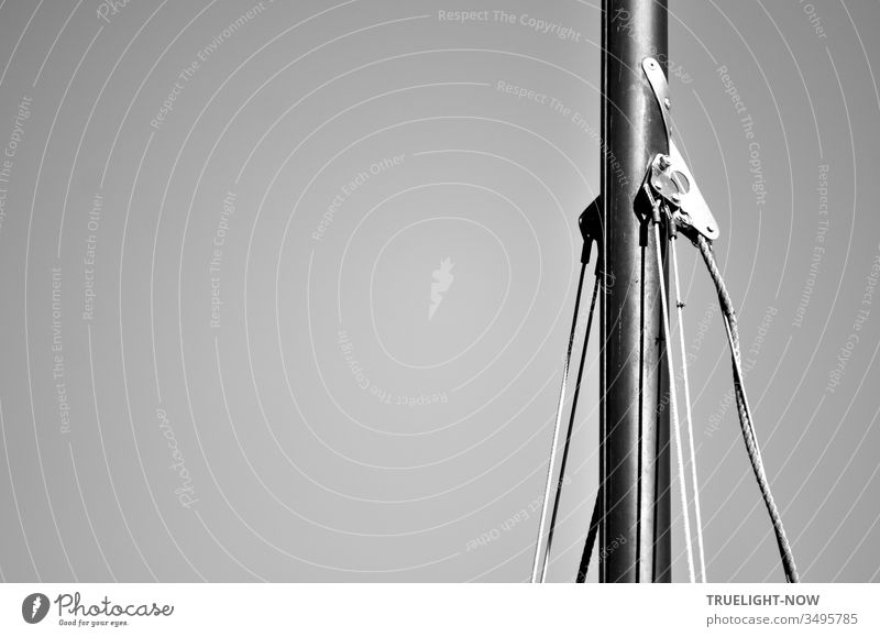 Der Aluminium Mast einer alten Ixylon Segeljolle mit Wanthänger und Wanten in Teilansicht schwarz-weiß vor dem neutralem Hintergrund eines wolkenlosen Himmels