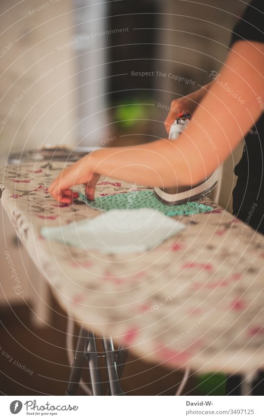 Frau bügelt Stoff mit einem Bügeleisen auf einem Bügelbrett bügeln coronavirus Mundschutz Mundschutzmaske selfmade Hausfrau Hausarbeit Starke Tiefenschärfe