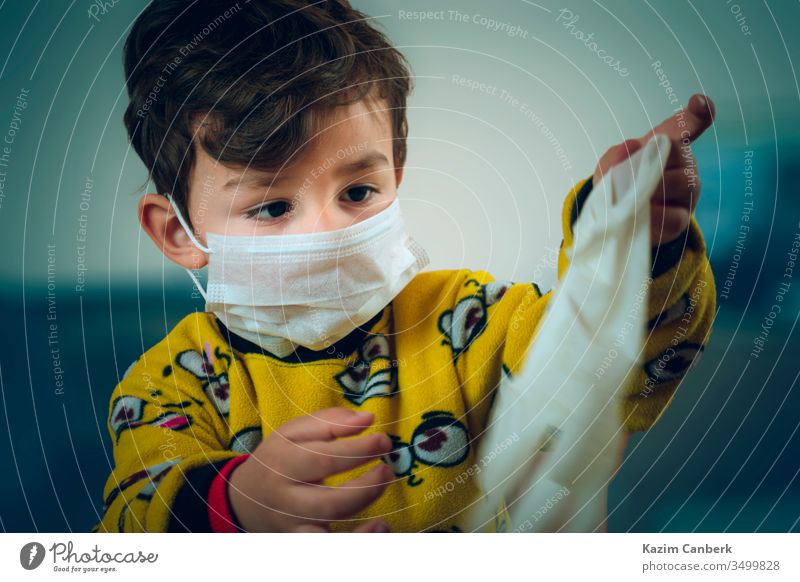 Glücklich aussehendes 3 Jahre altes Baby in Pyjama und Maske spielt mit Operationshandschuhen Kind Handschuh Mundschutz Korona Virus Corona-Virus weltweit