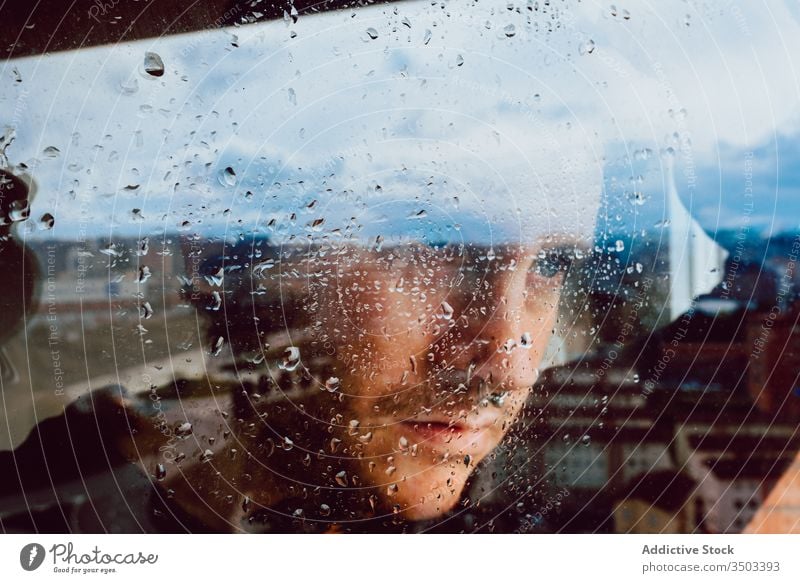 Depressiver Mann schaut durchs Fenster traurig Depression Isolation Coronavirus heimwärts verzweifelt einsam unglücklich jung männlich nass Regen Melancholie