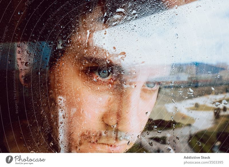 Depressiver Mann schaut durchs Fenster traurig Depression Isolation Coronavirus heimwärts verzweifelt einsam unglücklich jung männlich nass Regen Melancholie