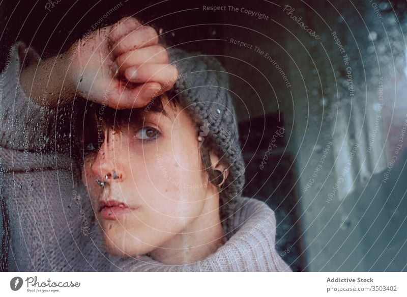 Melancholische junge Frau schaut durchs Fenster traurig Depression Isolation Coronavirus heimwärts verzweifelt einsam unglücklich männlich nass Regen