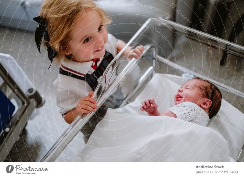 Glückliches Mädchen steht in der Nähe eines neugeborenen Geschwisters Baby Schwester Geschwisterkind schlafen Krankenhaus Babybett Wiege Kind wenig Pflege