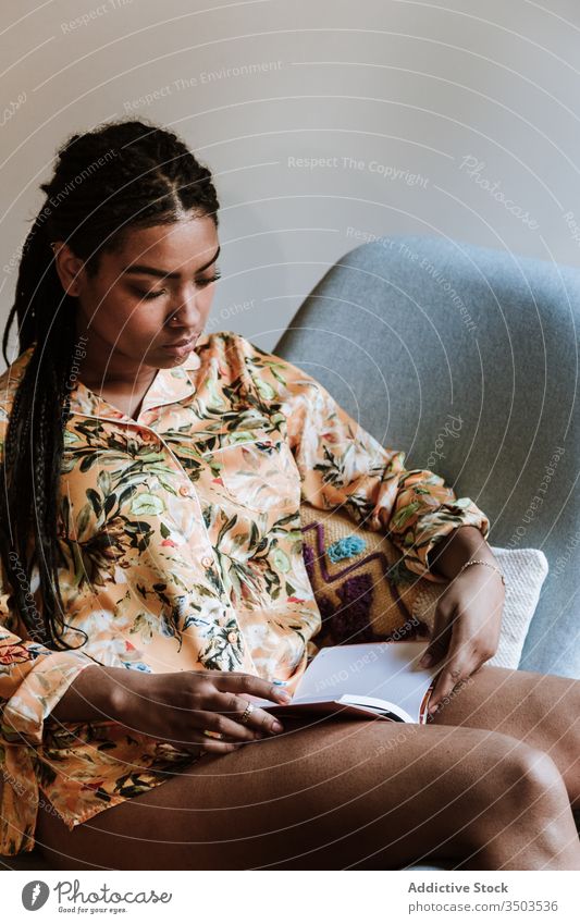 Ethnische Frau mit zu Hause ruhendem Buch heimwärts lesen Afrikanisch Amerikaner schwarz lässig Stuhl brünett Windstille Sitzen jung gemütlich ethnisch Freizeit