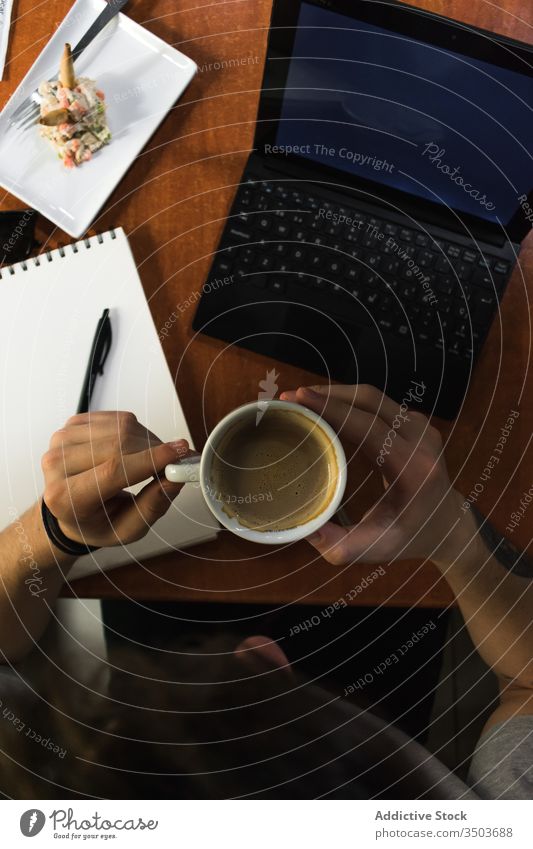 Freiberufler, der an einem Café-Tisch sitzt und Kaffee trinkt Mann Skizze Notebook freiberuflich Laptop abgelegen Projekt männlich zeichnen Notizblock Tasse