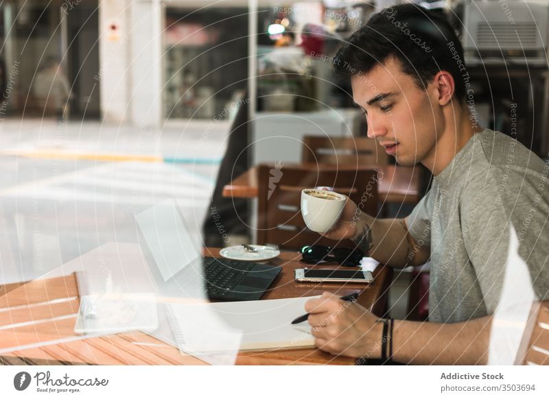 Student trinkt Kaffee und macht Notizen im Café Mann Schüler schreiben Hinweis Notebook jung Bildung trinken männlich Kantine Tasse Tisch Fenster Restaurant
