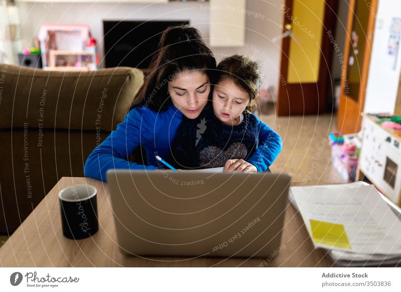 Mutter mit Tochter arbeitet an Fernprojekt freiberuflich Arbeit heimwärts Umarmung lesen Papier Laptop Tisch Frau Mädchen beschäftigt Projekt Kind Zusammensein