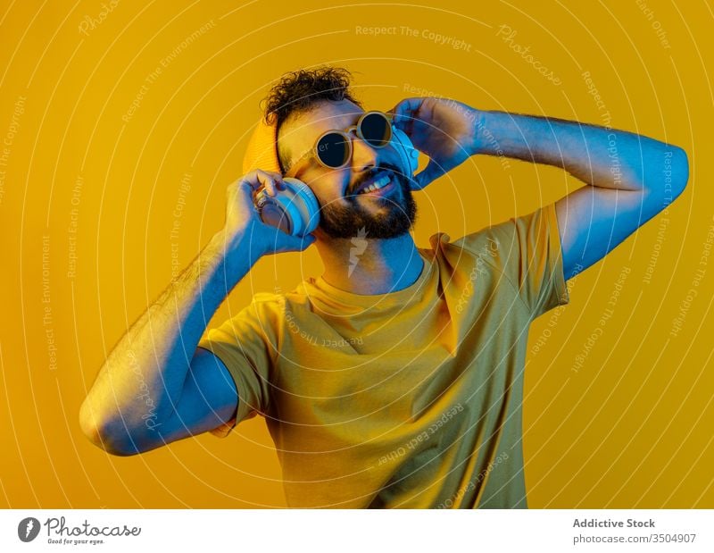 Bärtiger Mann mit modernen Kopfhörern urban Stil Outfit Musik Farbe hell männlich Zeitgenosse weiß gelb Accessoire Hut Sonnenbrille Klang Melodie lebhaft