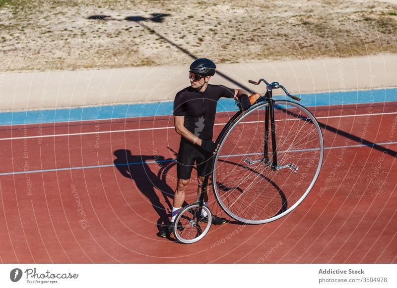 Nachdenklicher erwachsener Sportler mit Hochrad im Sportstadion Mann Fahrrad Stadion Radfahrer Pfennigfuchser Sportpark passen Reiter Training Athlet sportlich