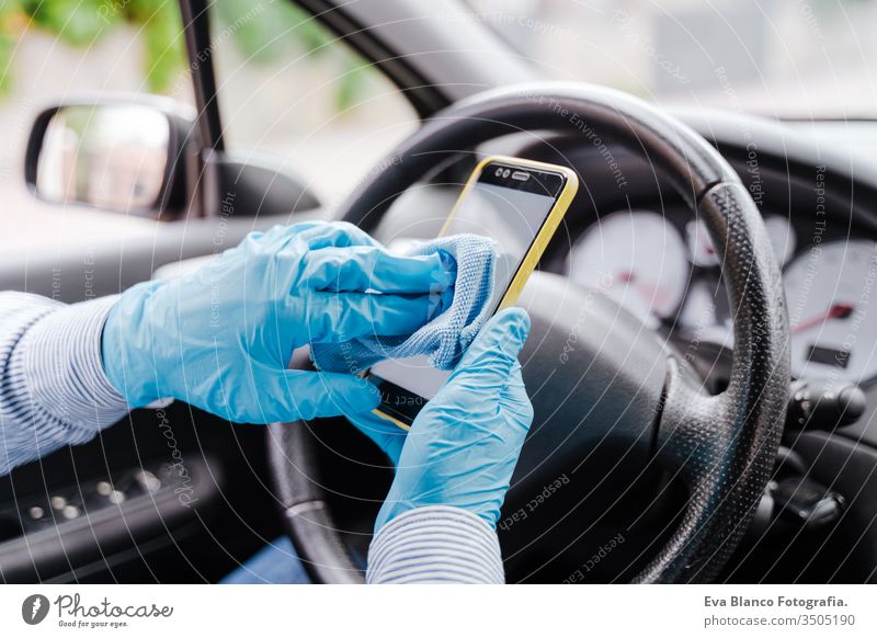 mann desinfiziert mobiltelefon mit alkoholgel in einem auto mit schutzmaske und handschuhen während der pandemie des coronacirus covid-19 Mann fahren PKW