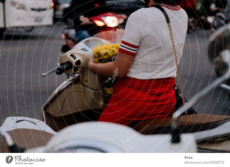 Eine elegant gekleidete Frau auf einem Roller im Straßenverkehr mit einem Strauß gelber Blumen im Arm urban Blumenstrauß Transport rot Großstadt Verkehr modern