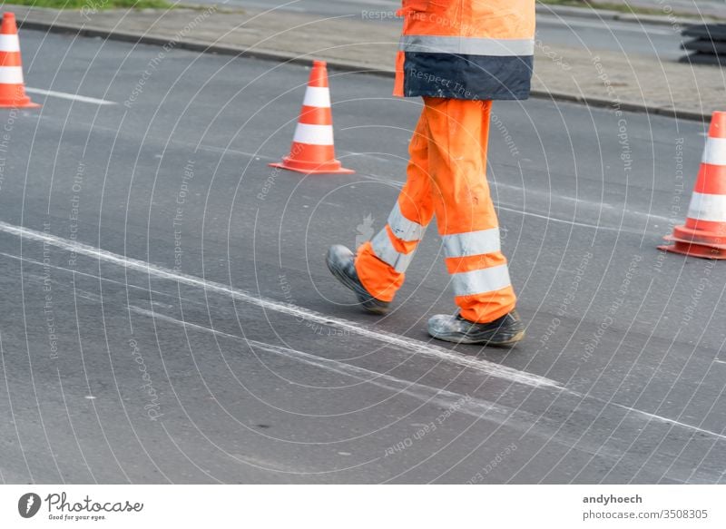 Straßenarbeiter geht auf der Straße mit Kegeln im Hintergrund Asphalt Asphaltierung Aufmerksamkeit Barriere Zapfen Konstruktion Textfreiraum Gefahr Gerät