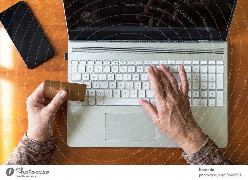 Draufsicht auf die Hände einer alten Frau, die mit einer Kreditkarte und einem Laptop zu Hause online einkauft. Konzept von alten Menschen und Technik. bezahlen