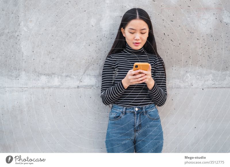 Asiatische Frau, die ihr Mobiltelefon benutzt. grau Wand Mobile asiatisch Asien Japanisch Chinesisch Mädchen Telefon Koreaner Funktelefon klug jung Smartphone