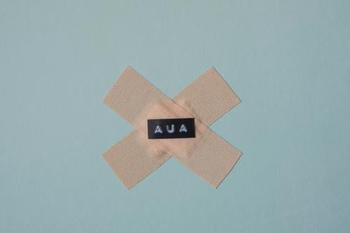 Zwei Pflaster auf denen das Wort Aua geschrieben steht; Schmerz, Verletzung verarzten Wunde Unfall Gesundheitswesen blau Hintergrund neutral Heftpflaster