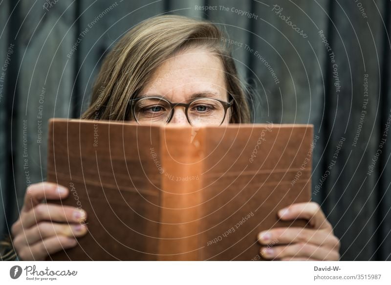 Frau mit Brille hält ein Buch in den Händen und liest lesen jung Leserin vertieft nerdig natürlich spannung Literatur Bildung konzentriert