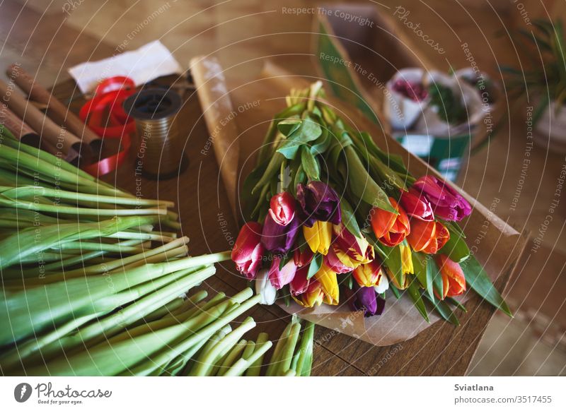 Ein riesiger mehrfarbiger Tulpenstrauß liegt auf einem Tisch in einem Blumenladen. Vorbereitung auf Frauentag und Valentinstag Blumenstrauß Hände Papier Ansicht