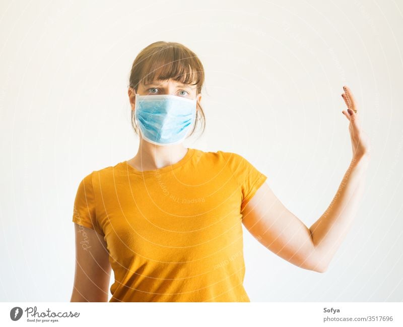 Junge Frau in Gesichtsmaske mit erhobenem Arm Coronavirus Mundschutz soziale Distanzierung Quarantäne Hand stoppen vereinzelt COVID19 entfernt zu Hause bleiben
