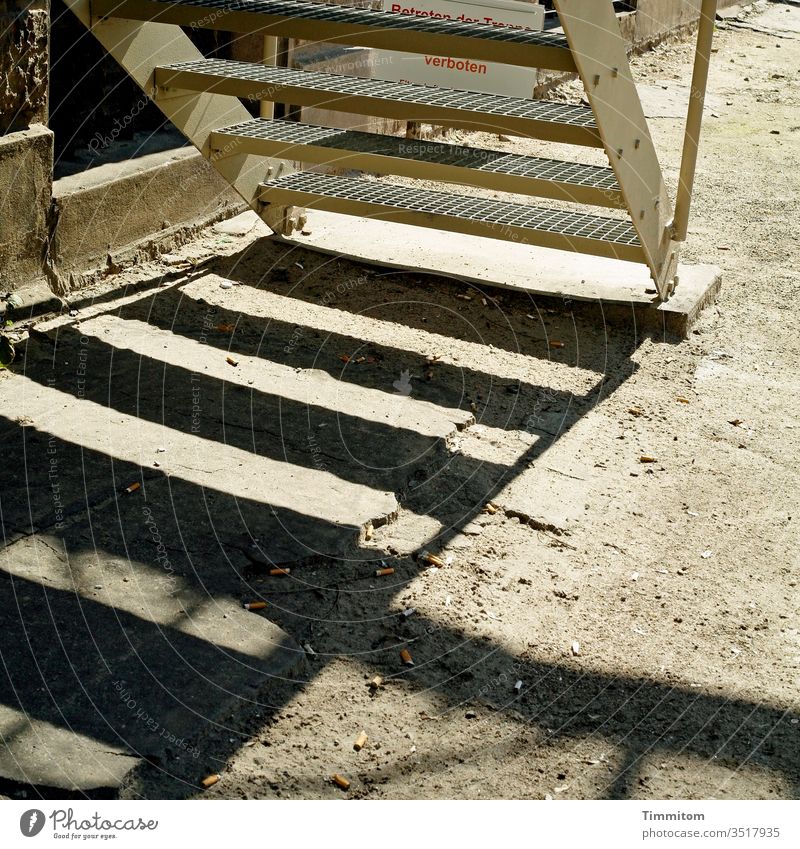 Treppe-Stufen-Schatten Metall Gitterroststufen Gebäude Wand Boden Sand Platten Zigarettenstummel Menschenleer Außenaufnahme trist Hinweisschild Verbotsschild