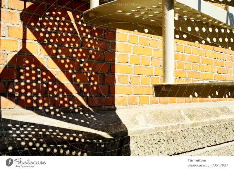 Treppe-Stufen-Schatten (2) Treppenstufen Metall Lochblech Löcher Gebäude Wand Ziegelsteine Fundament grell Menschenleer Farbfoto hell und dunkel aufwärts