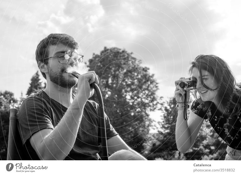 Mit einer Analogkamera fotografiert die Junge Frau ihren Bruder beim  Wasserpfeifenrauchen feminin Mensch Junger Mann maskulin fotografierend rauchend Rauch