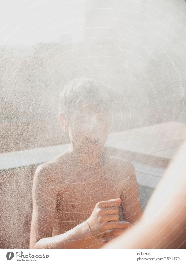 Fröhlicher junger Mann genießt eine Dusche mit dem Schlauch auf der Terrasse Junge Wasser Garten Sommer außerhalb Kinder spielen Erfrischung eingießen Spaß