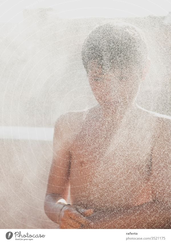Fröhlicher junger Mann genießt eine Dusche mit dem Schlauch auf der Terrasse Junge Wasser Garten Sommer außerhalb Kinder spielen Erfrischung eingießen Spaß
