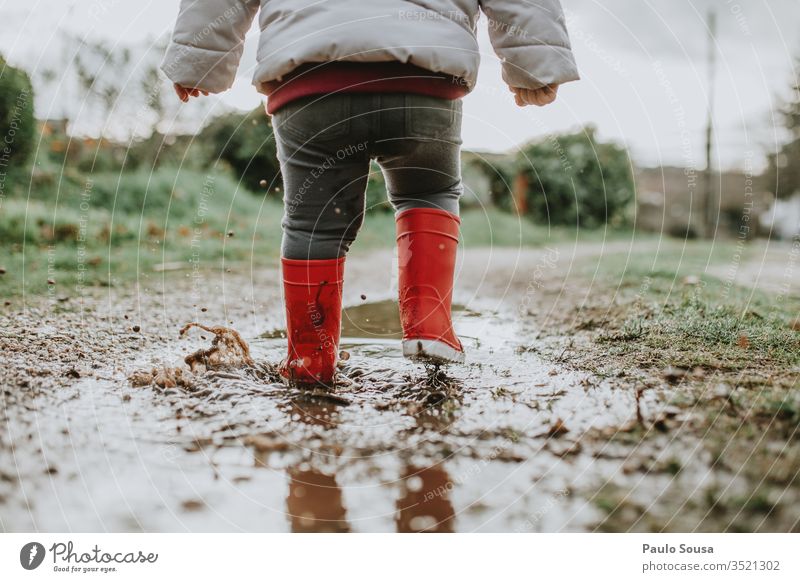 Untere Sektion eines Mädchens, das während der Regenzeit auf einer Pfütze läuft Kind Wasser Reflexion & Spiegelung Außenaufnahme rot Gummistiefel Kindheit