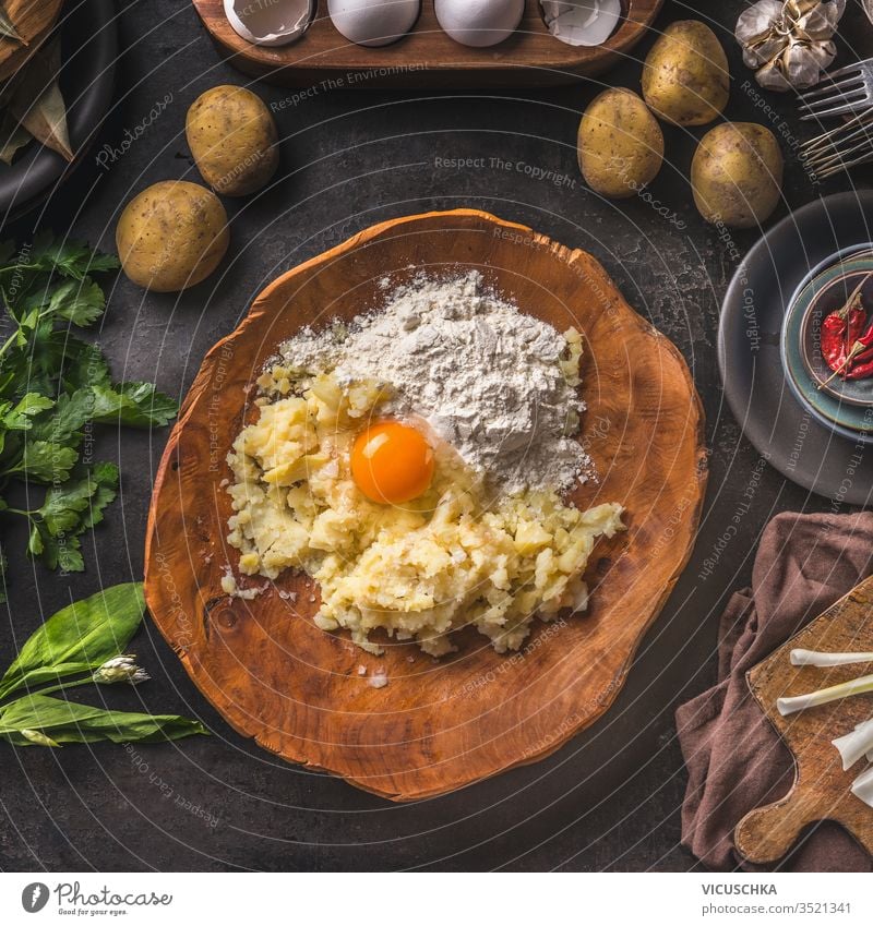Gnocchi-Teigzutaten. Kartoffeln mit Ei und Mehl in Holzschüssel auf dunklem Küchentisch mit biologischen Zutaten für die schmackhafte Hausmannskost. Zubereitung von Speisen. Rahmen. Ansicht von oben. Vintage-Küche