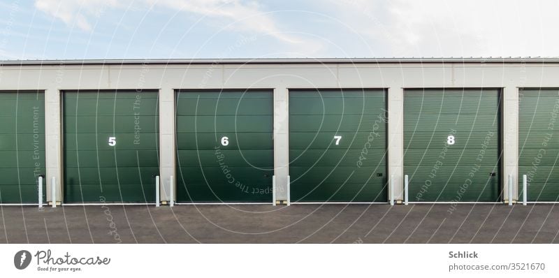 Nummerierte grüne Garagentore mit Nummern 5 6 7 8 frontal nummeriert Himmel hellblau Asphalt Rolltore geschlossen zu Blechdach Flachdach Lager Gebäude