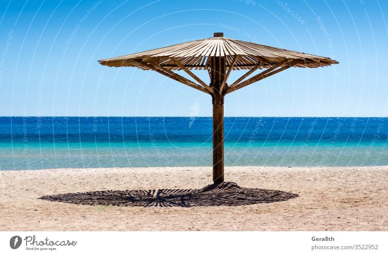 ein hölzerner Sonnenschirm auf dem Sand am Strand gegen das blaue Wasser des Roten Meeres in Ägypten Dahab Süd-Sinai Rotes Meer Hintergrund Strandhintergrund
