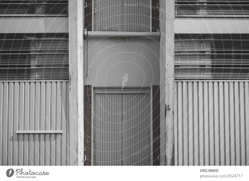 graue Fassade einer Lagerhalle Architektur Fabrik Gebäude Industrieanlage Tür Streifen Fenster Lagerschuppen lagern symmetrisch Symmetrie