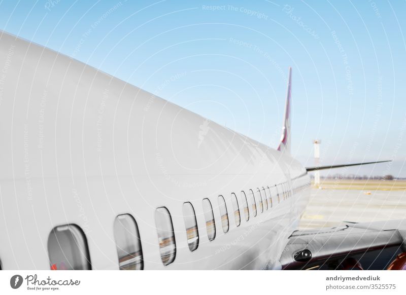 Bullauge des Flugzeugs - Seitenfenster in der Ebene. Weißes, schweres Passagierflugzeug mit Düsentriebwerk auf der Start- und Landebahn des Flughafens vor dem Hintergrund des blauen Himmels.
