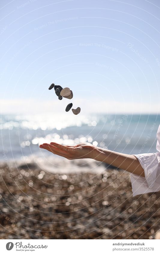 weibliche Hand wirft einen Kieselstein in die Hand vor dem Hintergrund des blauen Himmels, des Strandes und des Meeres. platz für text. Frau MEER Mädchen