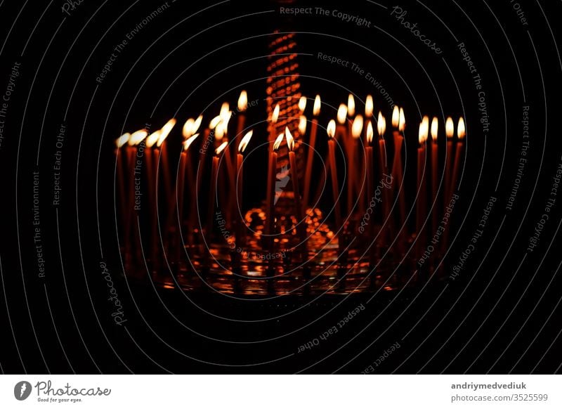 Viele Kerzen brennen nachts auf dem schwarzen Hintergrund in der Kirche. Kerzenflamme isoliert auf schwarzem Hintergrund gesetzt. Gruppe brennender Kerzen im Dunkeln