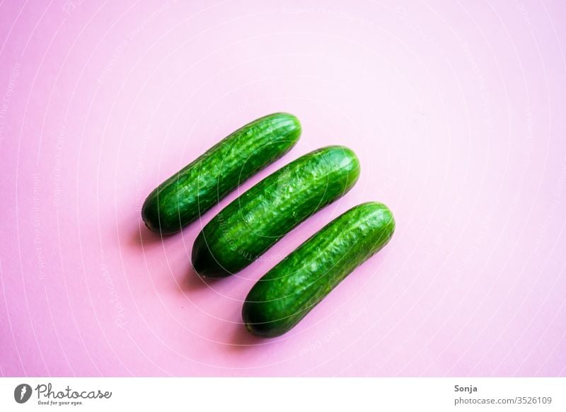 Drei kleine grüne Snack Gurken auf einem rosa Hintergrund, Draufsicht Gemüse Lebensmittel Ernährung Gesundheit frisch Vegane Ernährung Farbfoto