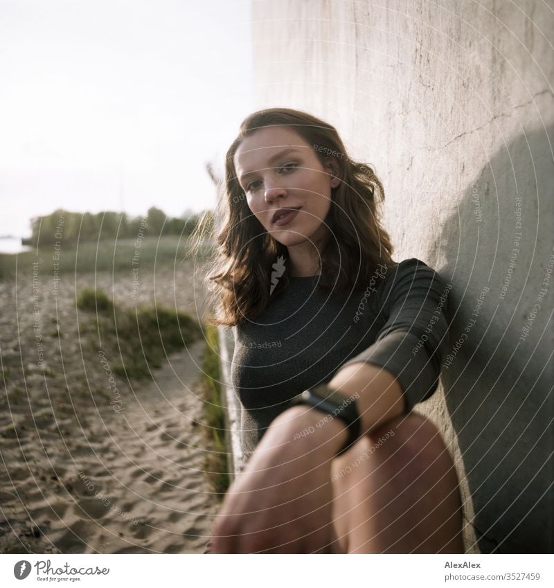 analoges Portrait einer jungen Frau im Kleid vor einer Wand Mädchen schön groß sportlich schlank fit brünett Locken langes Haar Beton Sand Strand Abend Körnung