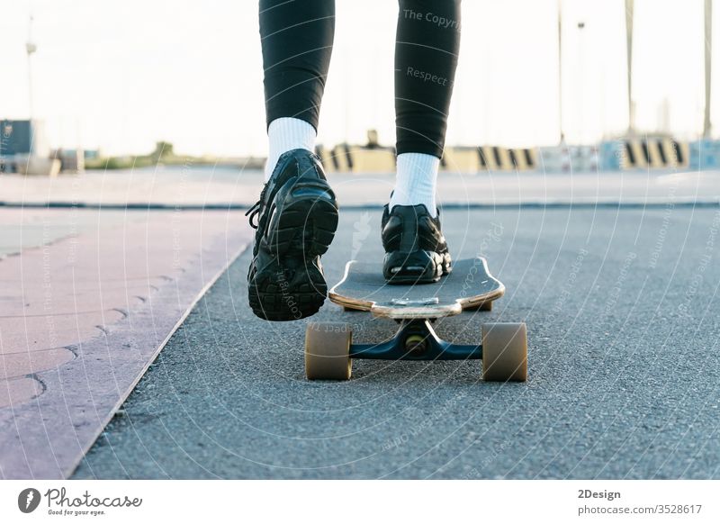 Eine nicht erkennbare Frau fährt auf einem Longboard um einen sonnenbeschienenen Park. abschließen genießen futuristisch Beine Besitzer Weg Mitfahrgelegenheit