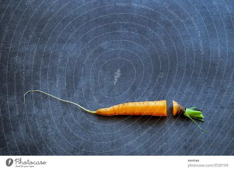 Möhre mit Schnitt und fehlendem Stück liegt quer auf dunkler Arbeitsplatte Karotte Karottengrün Lebensmittel Gemüse Bioprodukte Ernährung Vegetarische Ernährung