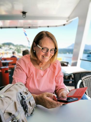 Ü70 Frau überprüft freudige Nachrichten auf dem Smartphone während einer Schifffahrt Seniorin pensioniert pensionärin bootsfahrt lachen Modus modisch verrotten
