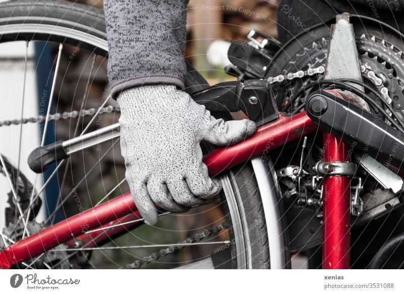 die behandschuhte Männerhand packte das Fahrrad nach der Reparatur am Rahmen und drehte es mit Kraft und Schwung herum Hand Fahrradkette Mann Fahrradrahmen