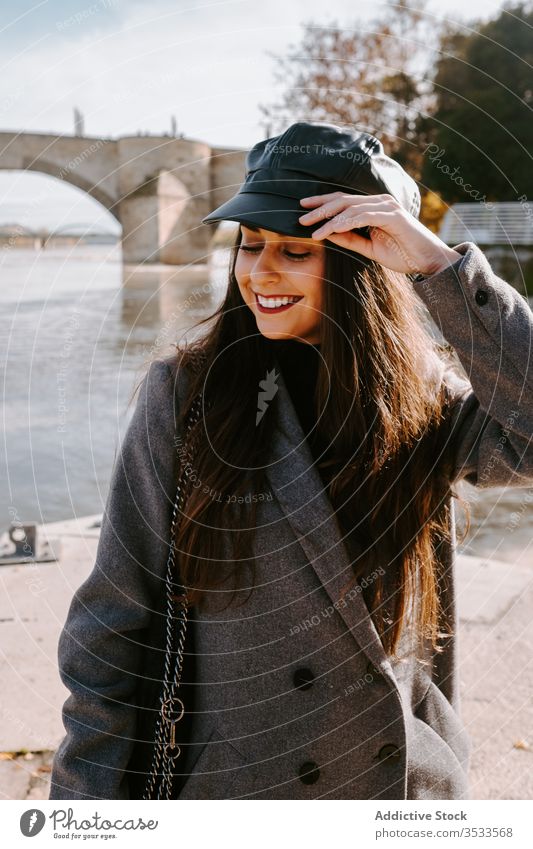 Fröhliche junge Frau auf der Böschung Stauanlage Fluss Lächeln Stil Oberbekleidung ausrichten Verschlussdeckel Glück trendy Kai Pier Augen geschlossen Wasser