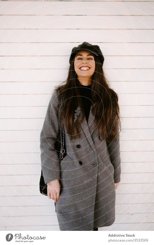 Selbstbewusste junge Frau an der weißen Wand Stil Straße selbstbewusst Verschlussdeckel Gebäude Mantel Outfit Model urban anhaben Accessoire Hut brünett
