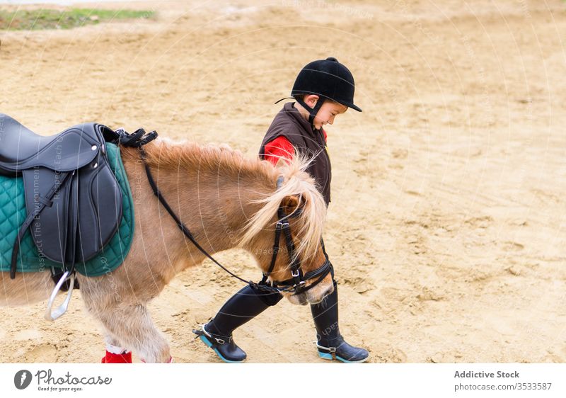 Glückliches kleines Jockey-Führungspony Junge Ponys Blei Arena Training Schule Reiterin Dressur Boden Schutzhelm Anzug Kind gehorsam loyal roan Sattel Zaumzeug