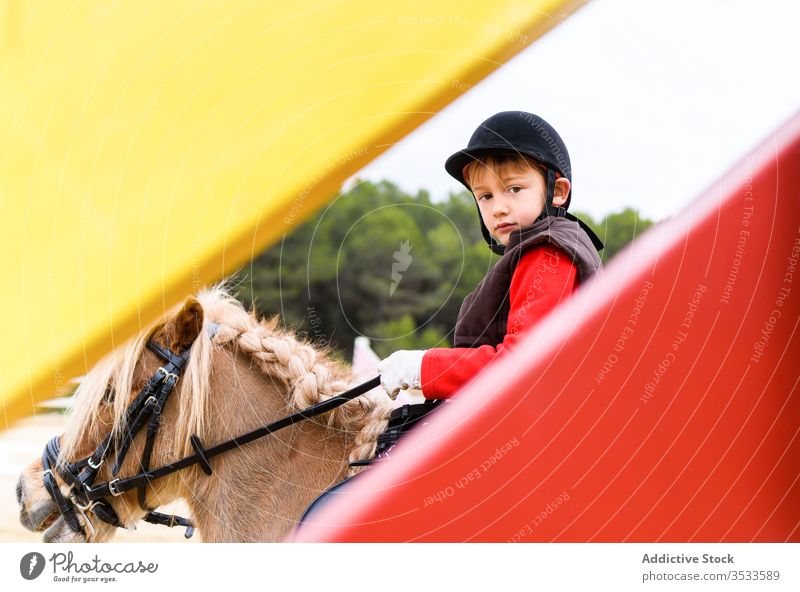 Junge reitet Pony hinter der Absperrung Ponys Mitfahrgelegenheit Jockey Arena Dressur Lektion Schule Reiterin Schutzhelm Kind Uniform Sicherheit behüten Mähne