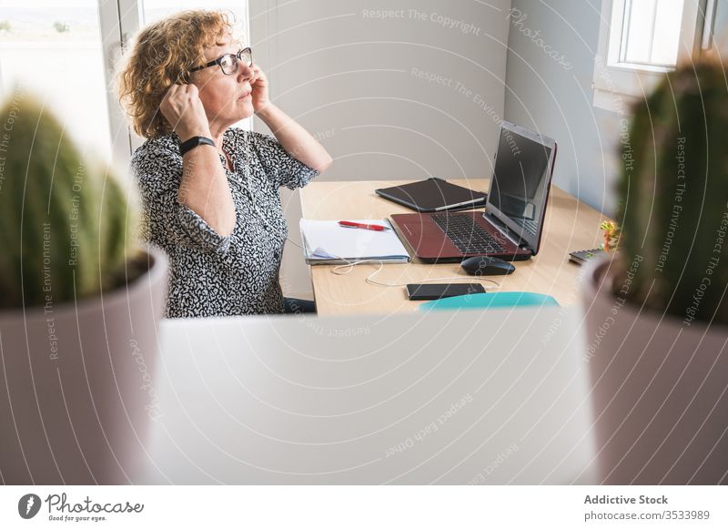 Erwachsene Frau arbeitet am Laptop in einem mit Kakteen in Töpfen dekorierten Raum Arbeit Pflanze benutzend freiberuflich Kaktus heimwärts Topf Kopfhörer