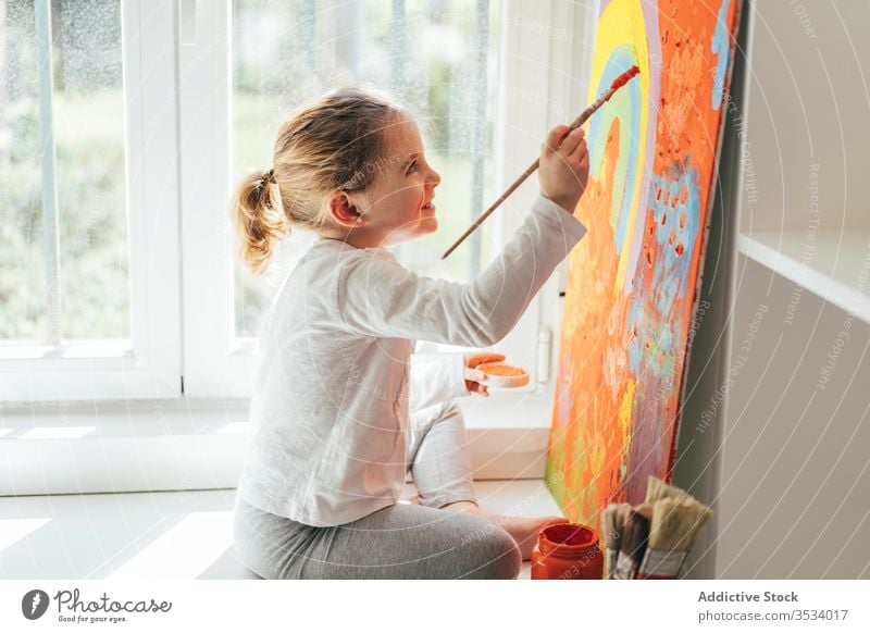 Kleines Mädchen malt Bild mit Pinsel Leinwand zeichnen Farbe Pinselblume Regenbogen Malerei kreativ farbenfroh orange Fensterbrett lässig Kunst Hobby