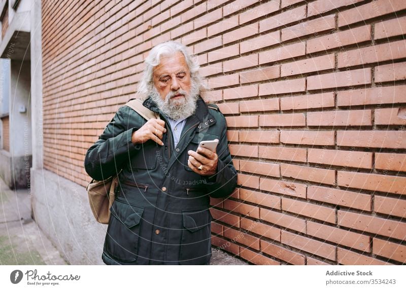 Männlicher Hipster mit Mobiltelefon an einer Backsteinmauer Senior Mann Smartphone Großstadt ernst Backsteinwand Straße benutzend männlich älter gealtert Lehnen