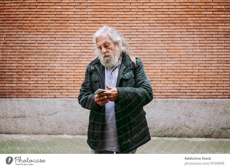 Männlicher Hipster benutzt Mobiltelefon in der Nähe einer Ziegelmauer Senior Mann Smartphone Großstadt ernst Backsteinwand Straße benutzend männlich älter