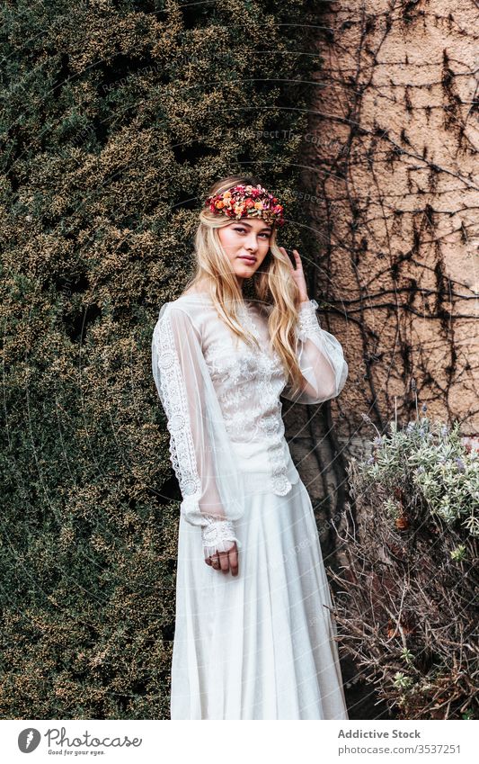 Junge Braut steht neben altem Anwesen Frau Haus Hof Buchse Wein Flora elegant Hochzeit jung Kleid Totenkranz gealtert eingetopft Blume Stil feiern Gelassenheit